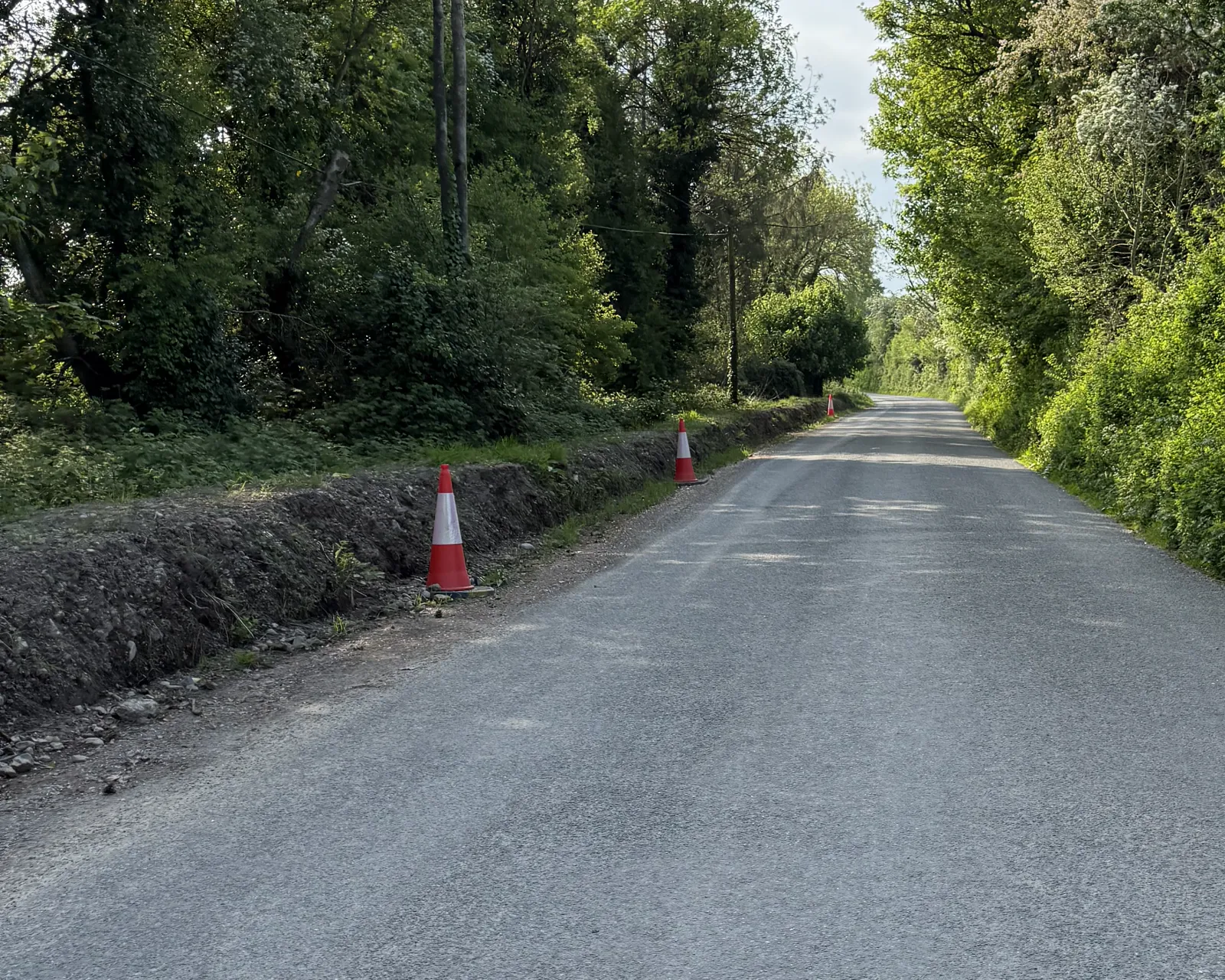 Context view of the left-hand roadside excavation/open line; drainage function unproven.